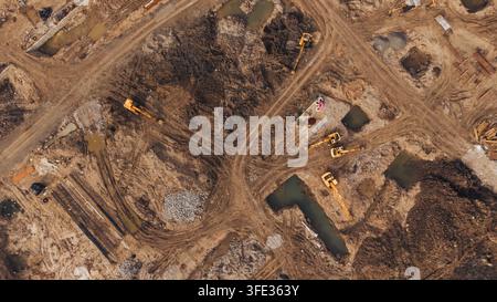 Aerial view of a construction site featuring multiple excavators working on muddy ground with pools of water and piles of debris in India. Stock Photo