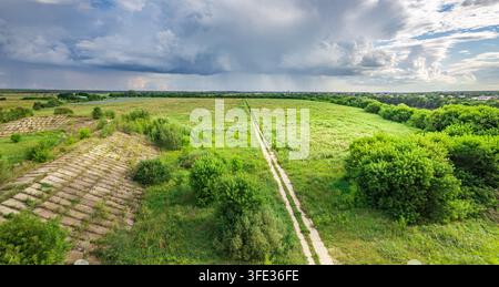 Vast green fields stretch under a dramatic sky. Winding path invites exploration through grassy terrain Stock Photo
