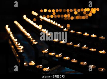 Tealight candles arranged in row in dark church Stock Photo