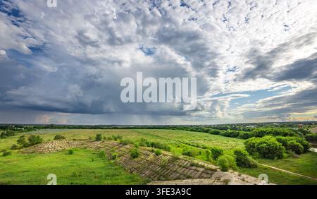 Vast green fields stretch under a dramatic, cloud-filled sky Stock Photo