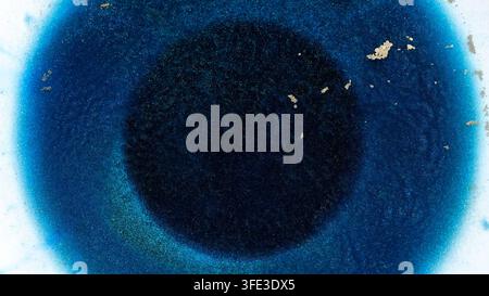Dark blue alcohol ink mixes slowly on a flat surface under bright light. The blend creates a unique pattern with hints of gold and lighter shades surr Stock Photo