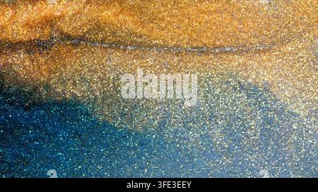 The process of mixing alcohol ink creates vibrant patterns and colors. Gold and blue swirl together in an artistic display, reflecting light and revea Stock Photo