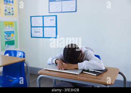 Closed silver laptop and black notebook are resting on wooden school desk in classroom Stock Photo