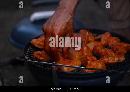 Close-up of unrecognizable hands coating raw chicken wings in spicy marinade before grilling on a barbecue. Food preparation concept for home cooking, Stock Photo