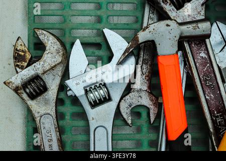 Close-up of used adjustable wrenches, hammer and measuring tools arranged on a green plastic tray in a workshop setting with visible rust and wear. Stock Photo