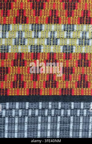 Close-up of handwoven mudmee ikat fabric with a red, yellow, black, and gray geometric pattern, photographed in Thailand. Stock Photo