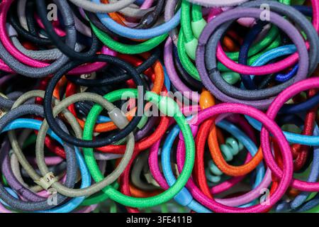 Top-down view of a dense, messy pile of multi-colored elastic hair bands and fabric accessories with plastic connectors, close-up texture. Stock Photo