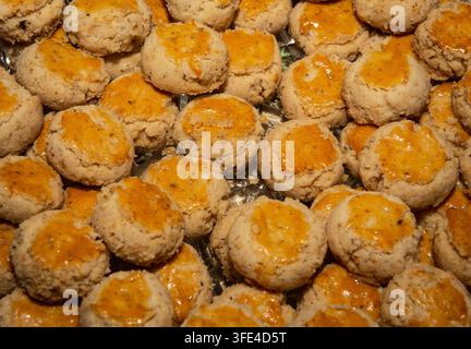 A top-down, close-up shot capturing a dense layer of golden-brown Chinese peanut cookies with glossy egg wash tops arranged on a clear serving platter Stock Photo