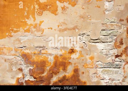 Close-up of a heavily weathered orange wall in Copenhagen, Denmark, with peeling plaster, exposed brickwork and irregular layers of decay creating a d Stock Photo