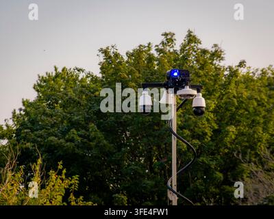 Modern surveillance cameras and security equipment mounted on a tall pole outdoors against trees Stock Photo