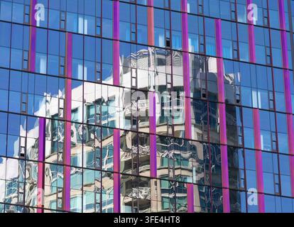 Modern glass building facade with colorful vertical accents and a distorted reflection of neighboring architecture across a geometric window grid. Stock Photo