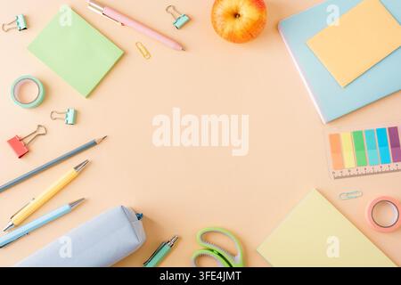 Pastel stationery arranged on a beige background with notebooks, pencils, pens, scissors, clips, tape and copy space. Top view, flat lay. Stock Photo