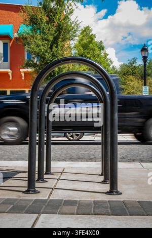 A curved metal bike rack stands on a sidewalk as a black SUV blurs past on a busy urban street. Stock Photo