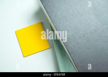 A minimalist top-down shot of a blank yellow sticky note placed next to a grey hardcover book on a light surface, ideal for office or educational conc Stock Photo