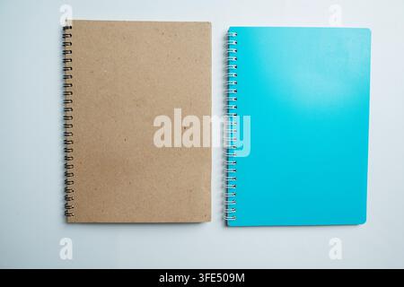 Top view of two blank spiral notebooks, one kraft brown and one bright blue, placed side-by-side on a light surface. Ideal for stationery, school, or Stock Photo