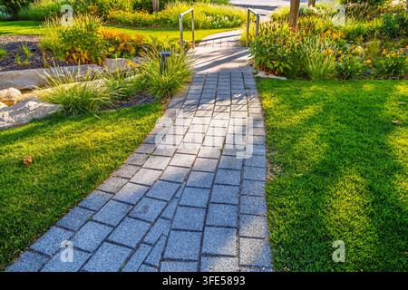 Stone pathway winding through a lush green garden with vibrant flowers and sunlight Stock Photo