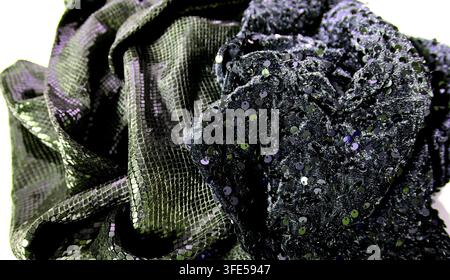 Close-up view of fabric textures showing shiny sequins on one piece and smooth patterned texture on another in bright light. The arrangement shows dar Stock Photo