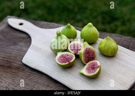 A beautiful rustic display of fresh figs, some whole and others sliced, beautifully arranged on a weathered wooden board for food styling. Stock Photo