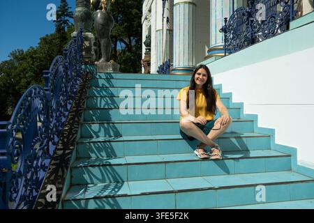 Young woman sitting cross-legged on sunny steps in front of historic architecture Stock Photo