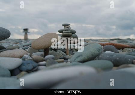 Carefully balanced rock stacks on a pebble beach under an overcast sky. Stock Photo