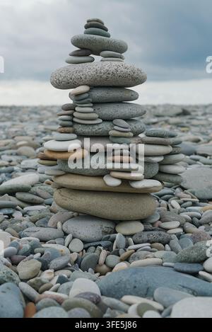 A close-up shot of a carefully balanced stack of smooth stones on a pebble-covered beach under an overcast sky. Stock Photo