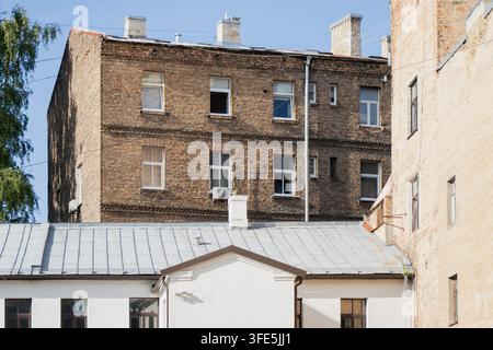 An old brick apartment building rises behind a tin rooftop, its weathered chimneys and rows of windows showing the patchwork repairs of a century-old Stock Photo