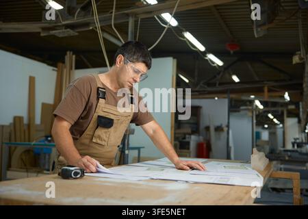 Workman assessing construction drawings in workshop while using measuring instruments and tools Stock Photo