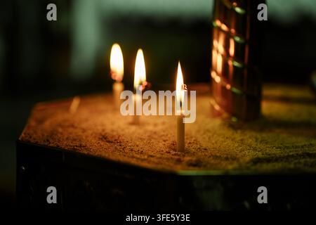 Three glowing candles standing in sand, creating a serene, warm, and spiritual atmosphere for prayer, meditation, or religious ceremonies Stock Photo