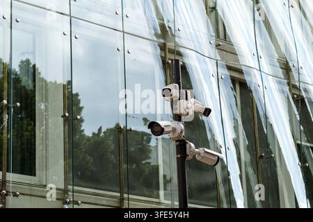 Cluster of security cameras on a pole positioned outside a contemporary glass architecture building, emphasizing surveillance and safety monitoring Stock Photo
