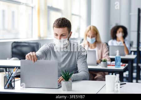 Coronavirus quarantine and office work with colleagues keeping social distancing. Portrait of young man in protective mask make video call with client Stock Photo