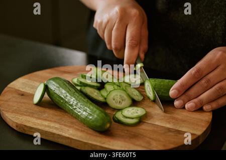 Hands of Woman Slicing Fresh Cucumbers on Cutting Board Stock Photo