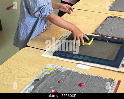 Close-up of a child's hands making handmade recycled paper using a screen frame and a sponge during a workshop. Stock Photo