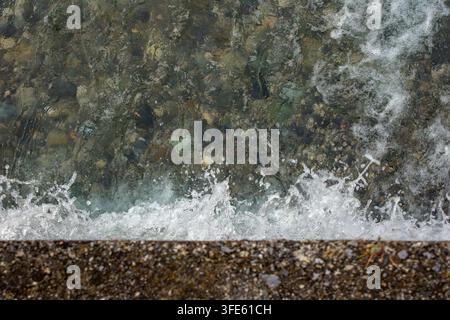 Foaming sea waves crash against a dark shoreline viewed from above. Surf represents water power, coastal nature and dynamic marine texture. Stock Photo