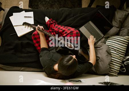 Woman Playing Guitar and Using Laptop for Online Music Lesson Stock Photo
