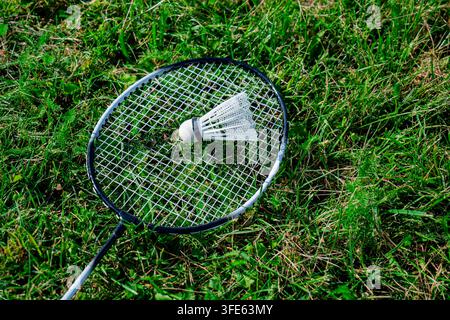 A single badminton racquet lying diagonally on a green lawn with a white birdie placed inside its head frame Stock Photo
