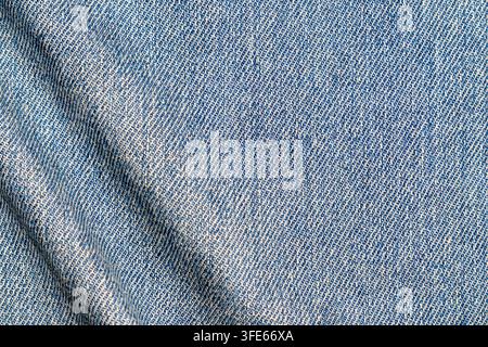 Top view of light blue denim jeans fabric texture with subtle folds and diagonal twill weave pattern. Seamless textile background ideal Stock Photo