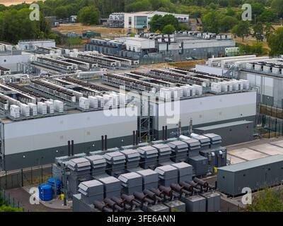 Aerial view of a large data center facility featuring rows of industrial cooling units, modern server buildings, and surrounding trees in the United K Stock Photo