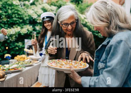 Happy women talking and sharing appetizers at outdoor party Stock Photo