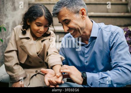 Happy senior man playing with his granddaughter while sitting on stairs Stock Photo