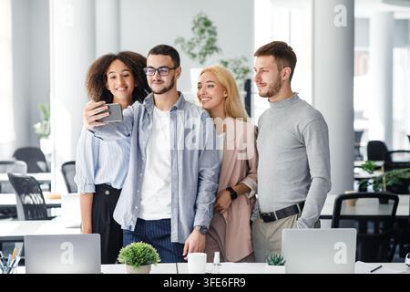 Multiracial workers looking at smartphone camera, guy makes photo in interior of modern office or video about company for clients Stock Photo