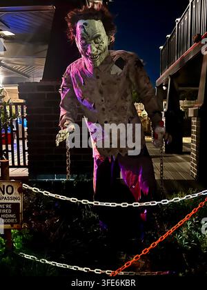 SAN DIEGO, CA - OCTOBER 28, 2025: Large creepy zombie prop animatronic with glowing eyes standing behind plastic chains as part of a residential Hallo Stock Photo