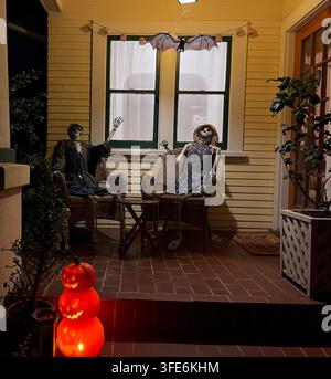 SAN DIEGO, CA - OCTOBER 28, 2023: Two dressed skeletons sitting in wicker chairs on a residential front porch beside jack-o-lantern pumpkins. Stock Photo