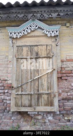 Closed old wooden shutters with rustic carved patterns and intricate carvings at the top. The shutters are antique and set against a brick wall backgr Stock Photo