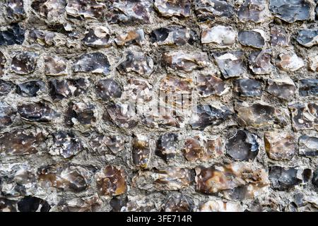 A detailed background texture showing rows of knapped knobbly flint stones set in mortar on an old building wall. Stock Photo