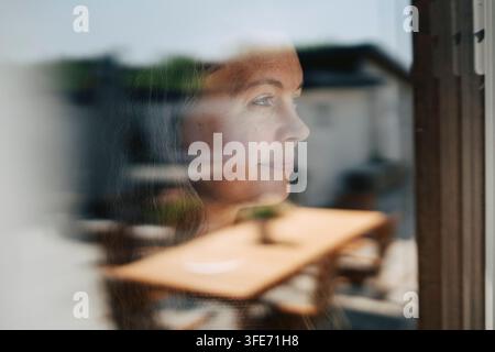 Smiling mature woman looking through glass window Stock Photo