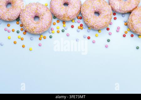 Pink doughnuts and candies on blue background, copy space flat lay Stock Photo
