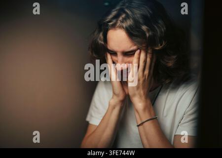 Frustrated young man touching his face seen in bathroom mirror Stock Photo