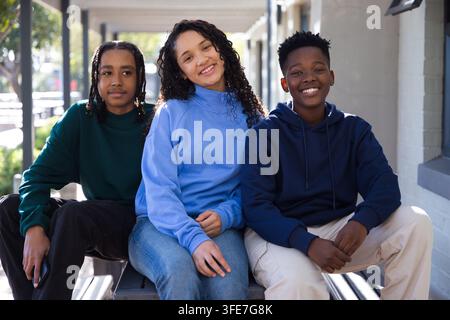 African American teens sitting and leaning forward on metal bench in covered walkway in sweatshirts Stock Photo