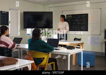 Diverse students and Indian presenter discussing code on screen with laptops in class, copy space Stock Photo