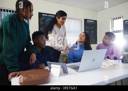 Indian woman instructor leading four teenage students around table in classroom with silver laptop Stock Photo